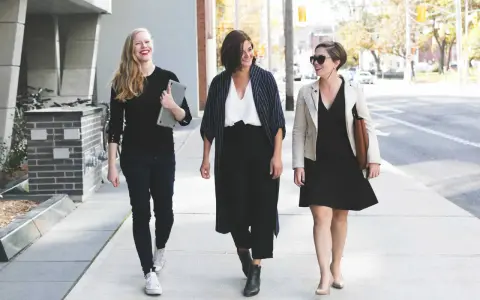 Tres mujeres con atuendo de negocios caminan por la acera, sonriendo y conversando.