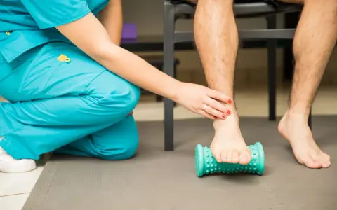 Fisioterapeuta ayuda a un paciente a aliviar el dolor de fascitis plantar con un rodillo de masaje.