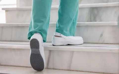 Persona subiendo escaleras con zapatos blancos, mostrando la suela antideslizante. El poliuretano en zapatos ofrece comodidad y durabilidad.