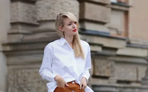 Mujer con falda de gamuza y camisa blanca, posando con las manos en los bolsillos.