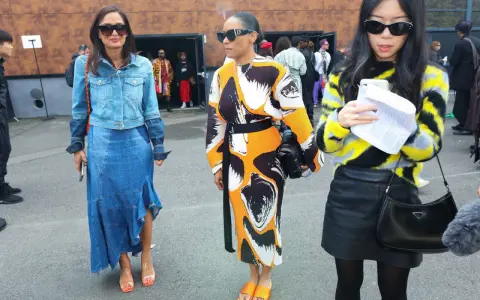 Tres mujeres posan con atuendos de moda. La del centro lleva un vestido estampado y sandalias naranjas, un ejemplo de que son mules.