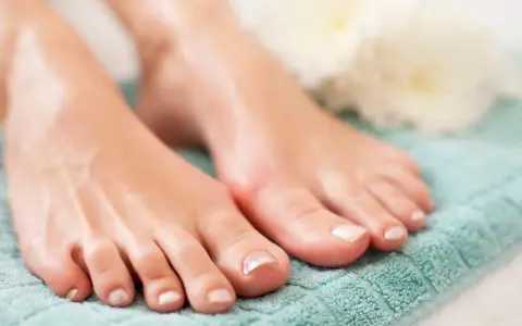 Pies cuidados con esmalte claro sobre toalla turquesa. El pedicura significado es cuidado y belleza para tus pies.