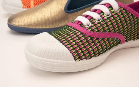 Zapatilla deportiva con malla verde y rosa, puntera blanca y suela vulcanizada. Al fondo, un zapato dorado y otro naranja.