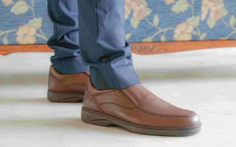 Un hombre viste pantalones azules y unos cómodos mocasines marrones, perfectos para cualquier ocasión.