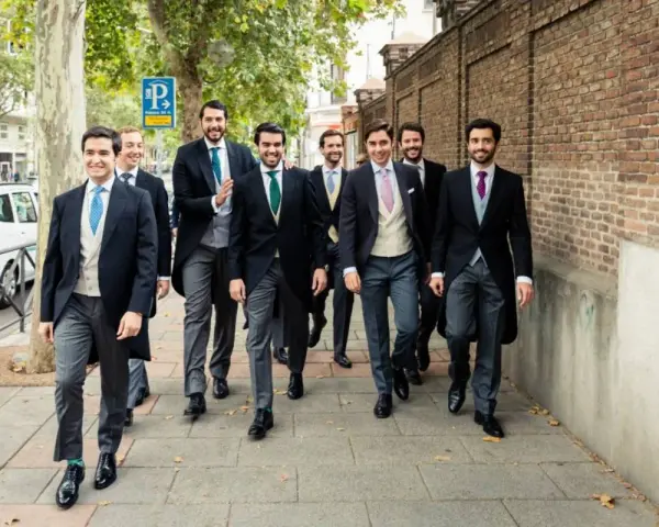 Un grupo de hombres camina por la acera, todos vestidos con trajes elegantes, cumpliendo el **código vestimenta** de un evento formal.