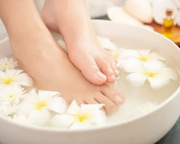 Pies sumergidos en agua con flores blancas, un ritual de spa para probar remedios caseros para quitar el mal olor de los pies.