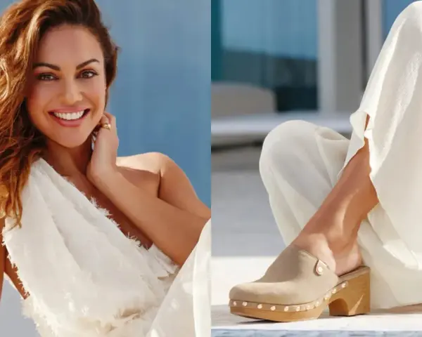 Mujer sonriente con vestido blanco y un pie calzado con zuecos de ante beige, adornados con tachuelas.