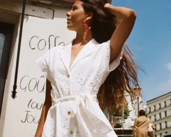 Mujer con un elegante outfit entrevista de trabajo verano, vestido blanco bordado, pendientes rojos, cabello suelto.