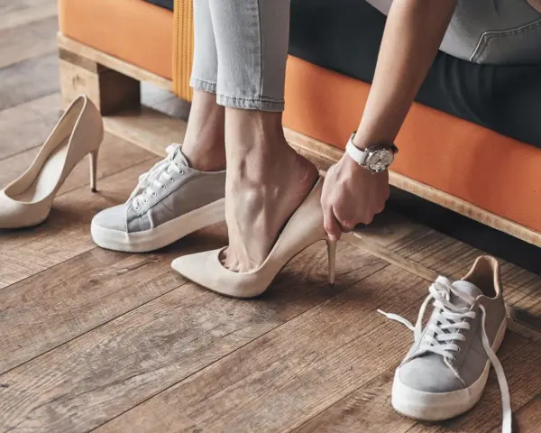 Persona se prueba unos tacones beige, rodeada de varios pares de zapatos. Se aprecian diferentes partes de un zapato, como la suela y el tacón.
