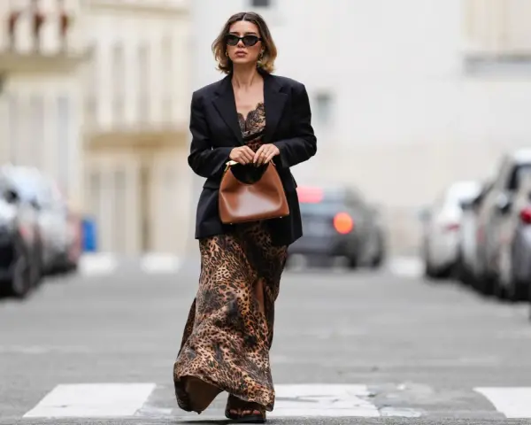 Mujer con un elegante outfit de domingo primavera: vestido largo de leopardo, blazer negro y bolso marrón.
