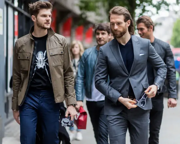 Hombres con estilo, uno con chaqueta y camiseta estampada, otro con traje gris. Dress code casual.