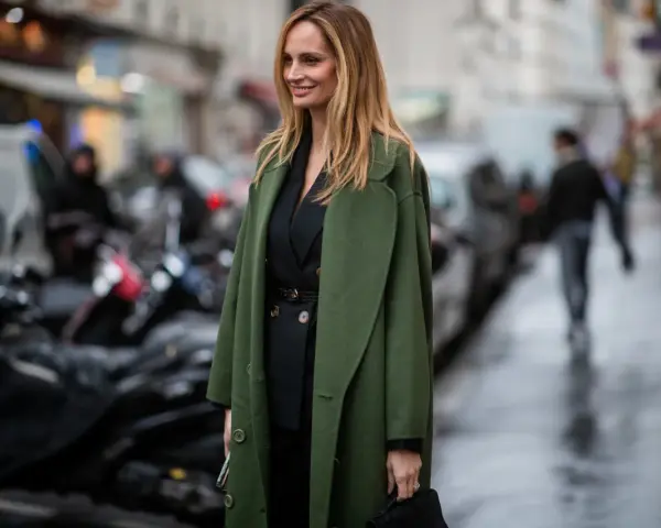Mujer con traje negro y un abrigo verde olivo, ideal para saber qué abrigo llevar con traje mujer.