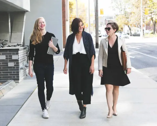 Tres mujeres con atuendo de negocios caminan por la acera, sonriendo y conversando.