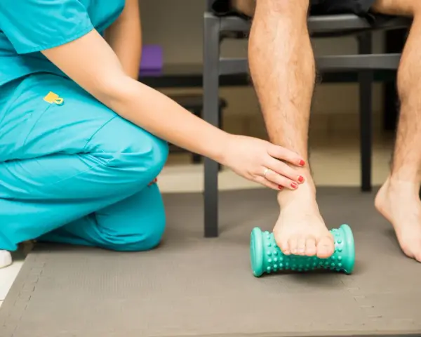 Fisioterapeuta ayuda a un paciente a aliviar el dolor de fascitis plantar con un rodillo de masaje.