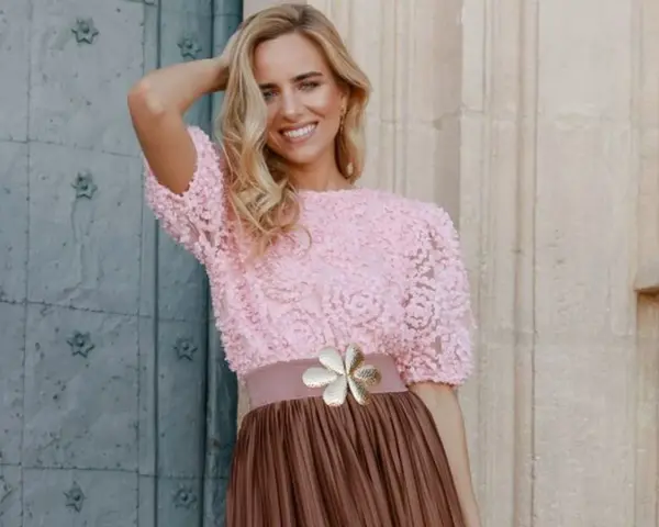 Mujer sonriente con top rosa de encaje y falda marrón, ideal para una boda en octubre, manga corta o larga.