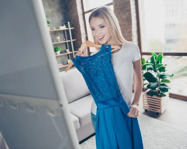 Mujer sonriente elige un vestido azul para un evento de dress code cocktail.