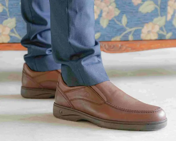 Un hombre viste pantalones azules y unos cómodos mocasines marrones, perfectos para cualquier ocasión.