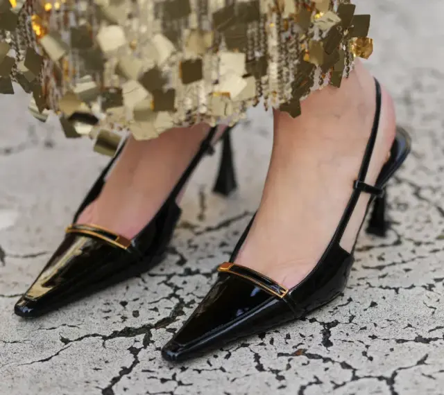 Elegantes zapatos pumps negros de charol con tiras al talón y detalle dorado.