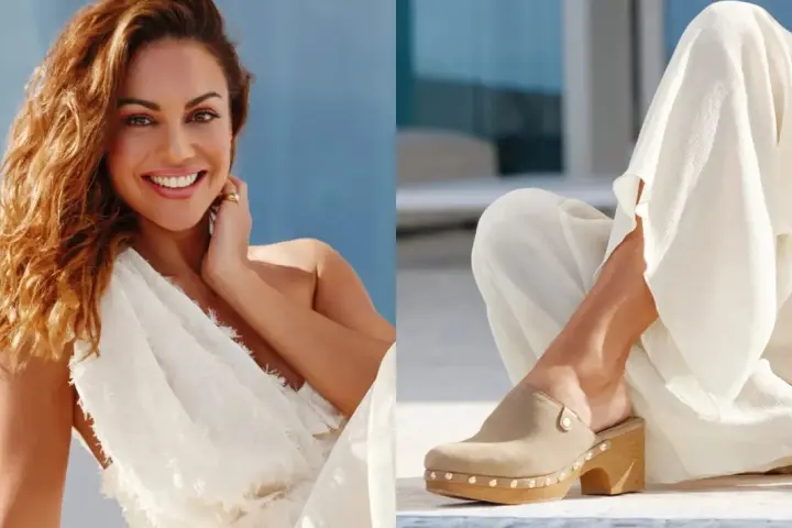 Mujer sonriente con vestido blanco y un pie calzado con zuecos de ante beige, adornados con tachuelas.