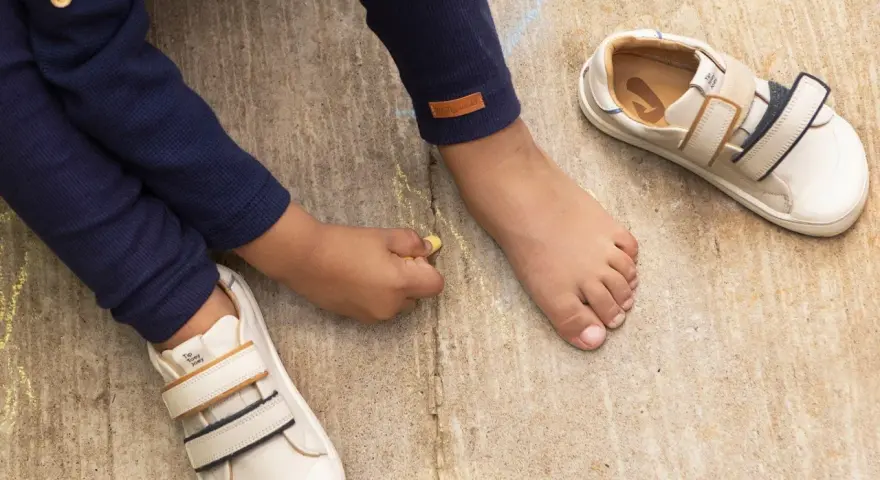 Niño descalzo dibuja con tiza junto a sus zapatos de calzado fisiológico, listos para la aventura.