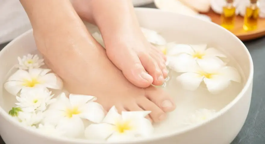 Pies sumergidos en agua con flores blancas, un ritual de spa para probar remedios caseros para quitar el mal olor de los pies.