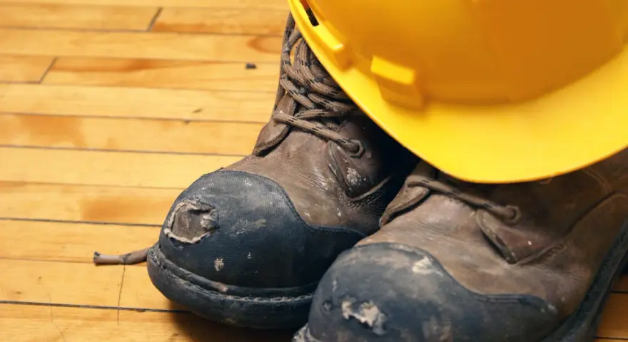 Botas de seguridad desgastadas y un casco amarillo, listos para lavar en lavadora.