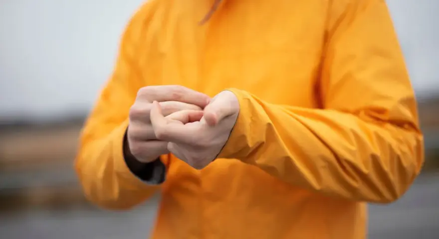 Persona se frota las manos dentro de una chaqueta naranja brillante. El poliéster da calor y protege del frío.