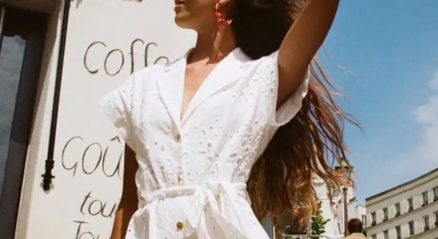 Mujer con un elegante outfit entrevista de trabajo verano, vestido blanco bordado, pendientes rojos, cabello suelto.