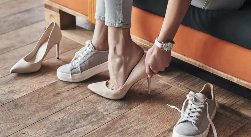 Persona se prueba unos tacones beige, rodeada de varios pares de zapatos. Se aprecian diferentes partes de un zapato, como la suela y el tacón.