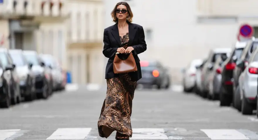 Mujer con un elegante outfit de domingo primavera: vestido largo de leopardo, blazer negro y bolso marrón.