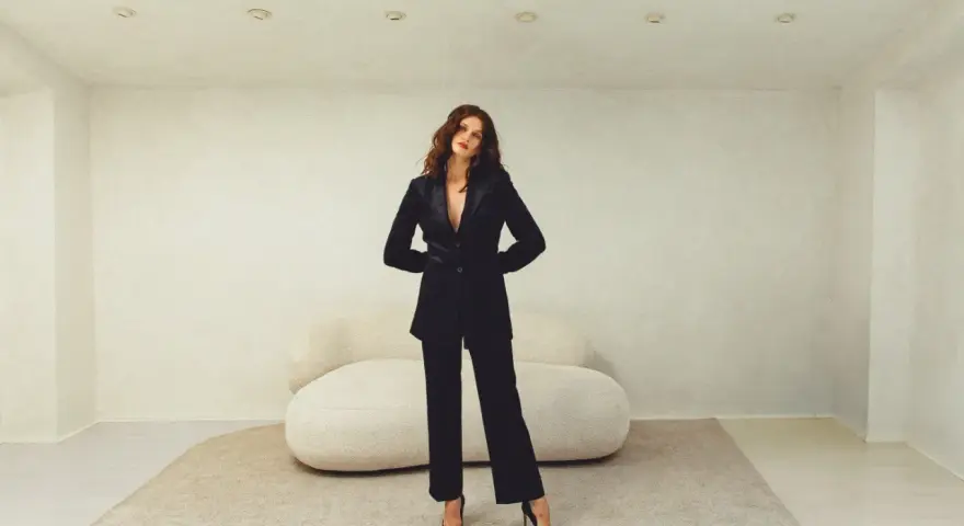 Mujer con elegante traje negro, parte de una colección de **monochrome outfits**. Posando con confianza en un estudio minimalista.