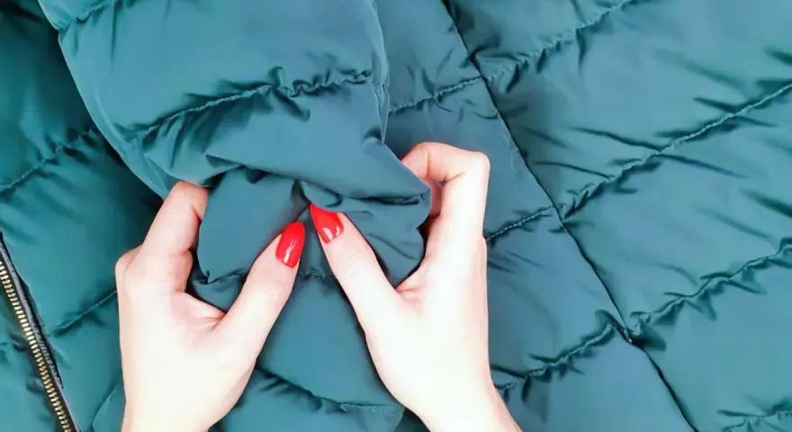 Manos con uñas rojas arrugan una chaqueta verde oscuro. ¡Por fin he lavado un plumas en la lavadora y está como nuevo!