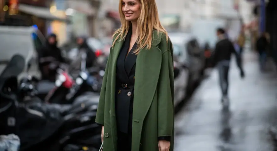Mujer con traje negro y un abrigo verde olivo, ideal para saber qué abrigo llevar con traje mujer.