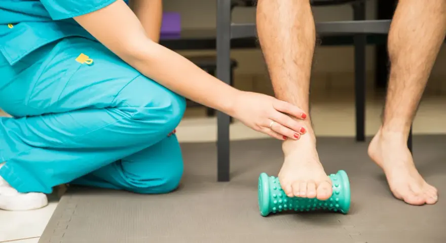 Fisioterapeuta ayuda a un paciente a aliviar el dolor de fascitis plantar con un rodillo de masaje.