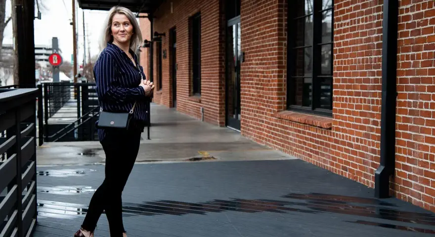 Mujer con outfit de camisa azul a rayas, pantalones negros y zapatos de tacón.