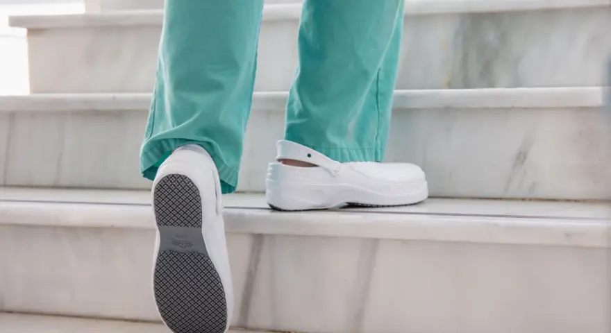 Persona subiendo escaleras con zapatos blancos, mostrando la suela antideslizante. El poliuretano en zapatos ofrece comodidad y durabilidad.