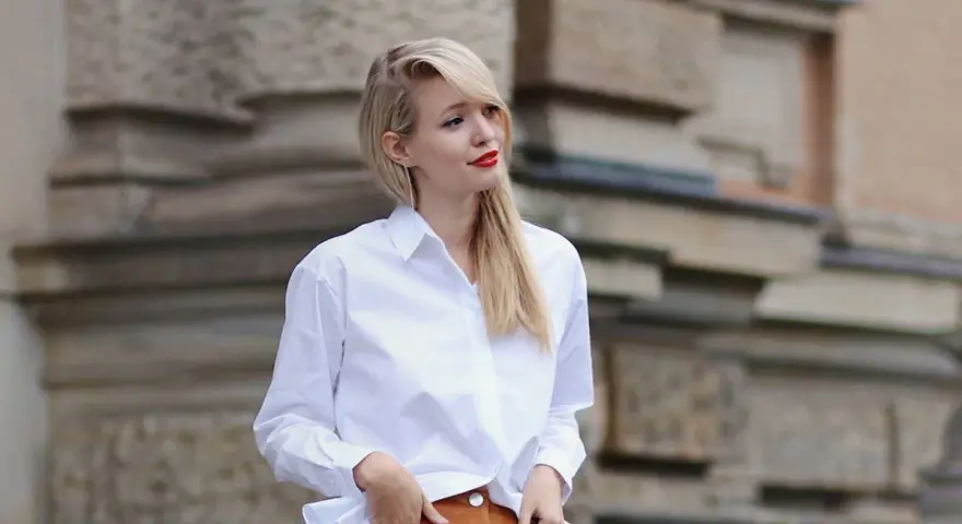 Mujer con falda de gamuza y camisa blanca, posando con las manos en los bolsillos.