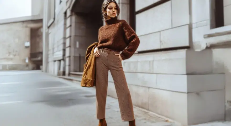 Mujer con suéter marrón y pantalones a rayas, luciendo un impecable estilo monocromático en la calle.