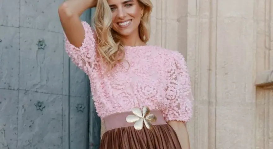 Mujer sonriente con top rosa de encaje y falda marrón, ideal para una boda en octubre, manga corta o larga.