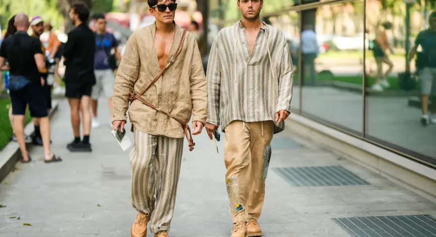 Dos hombres pasean con estilo. Uno lleva un kimono beige y pantalones de lino a rayas. El otro, una camisa a rayas y pantalones beige. Un ejemplo de cómo combinar pantalón lino beige hombre.