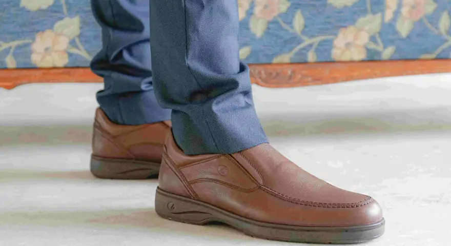 Un hombre viste pantalones azules y unos cómodos mocasines marrones, perfectos para cualquier ocasión.