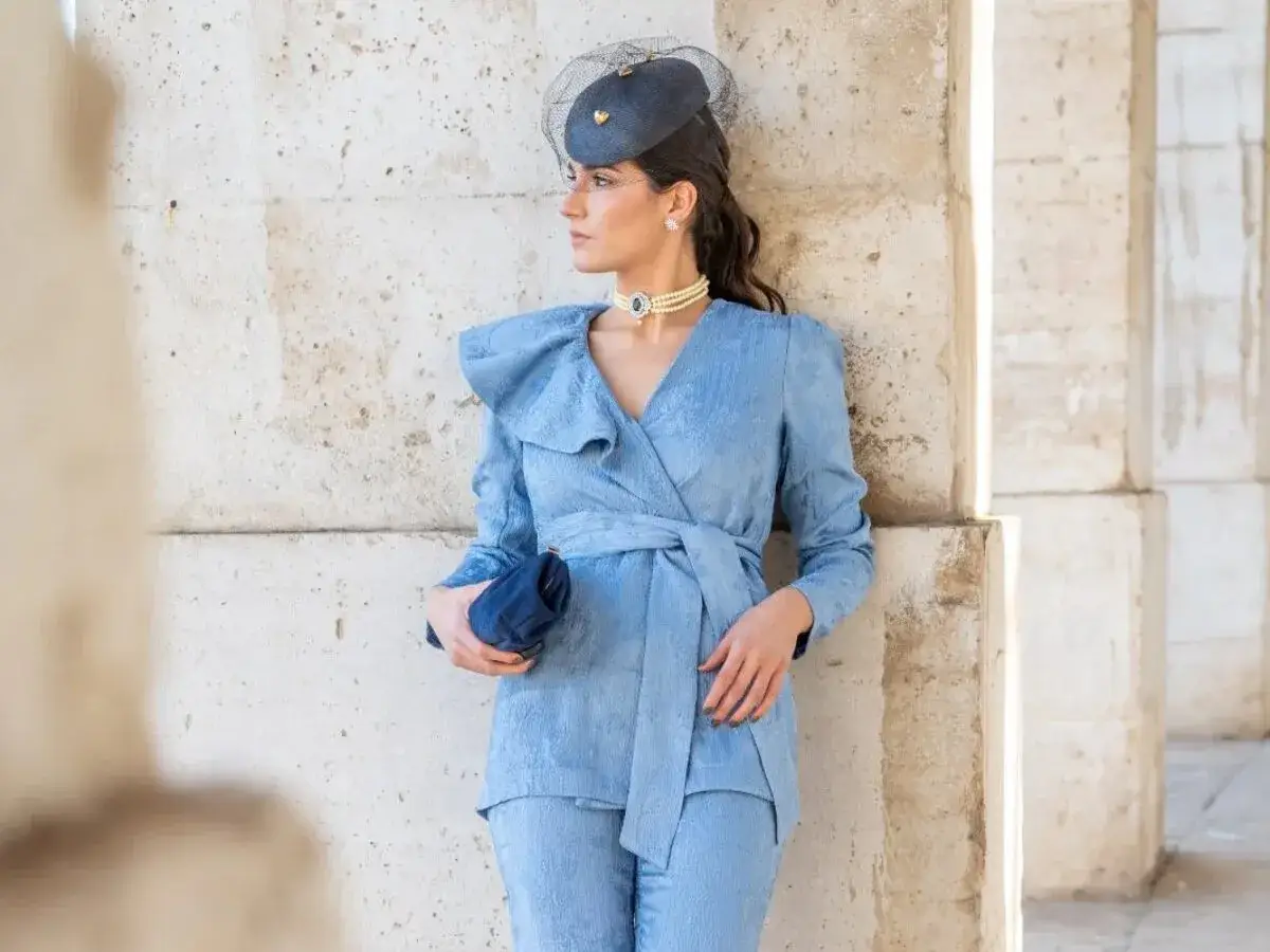 Mujer con traje azul claro, sombrero y bolso. Un ejemplo de que abrigo llevar con traje mujer para un evento elegante.