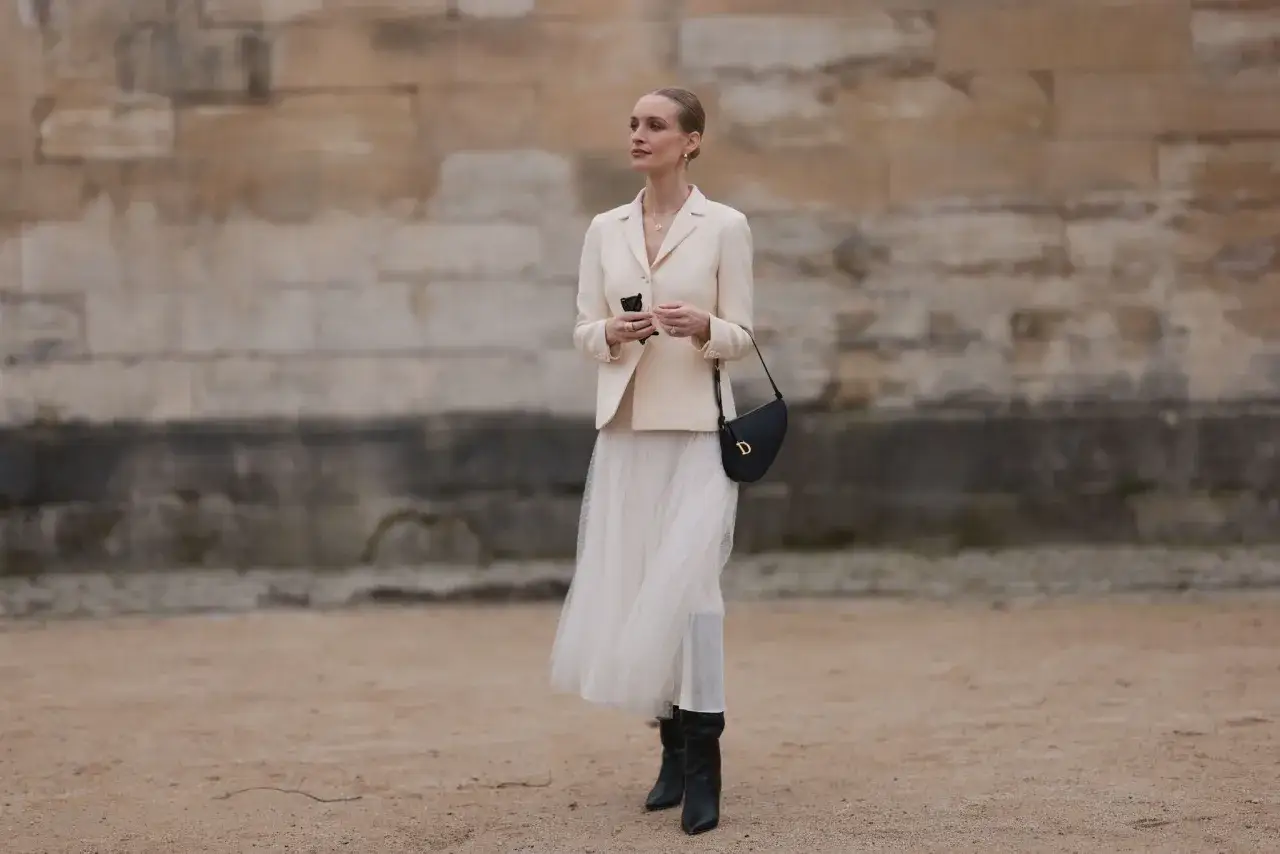 Mujer con vestido blanco vaporoso y chaqueta crema, combinando a la perfección con unas botas negras.