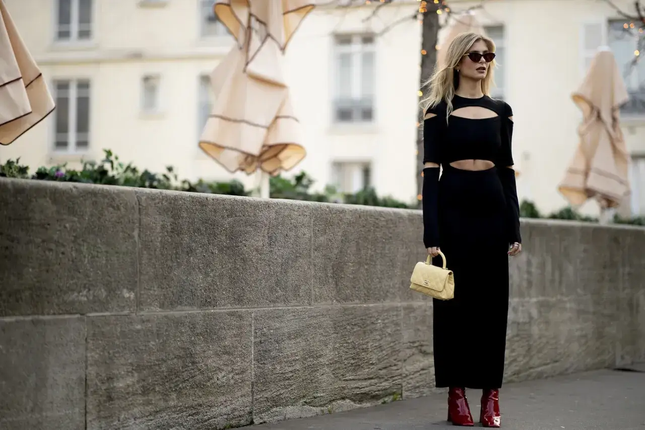 Mujer con vestido negro cut-out y botines rojos brillantes, lista para una fiesta.