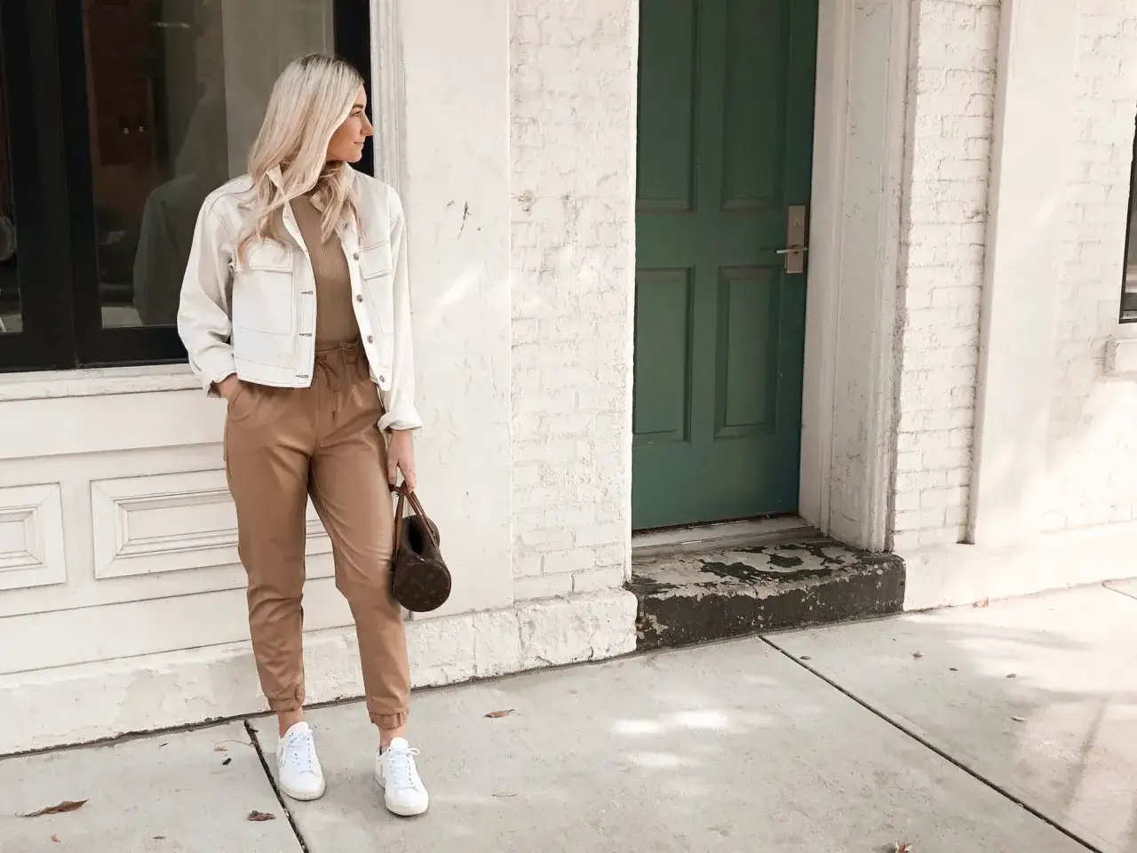 Mujer con estilo monocromático en tonos tierra, chaqueta blanca, pantalones camel y bolso marrón.