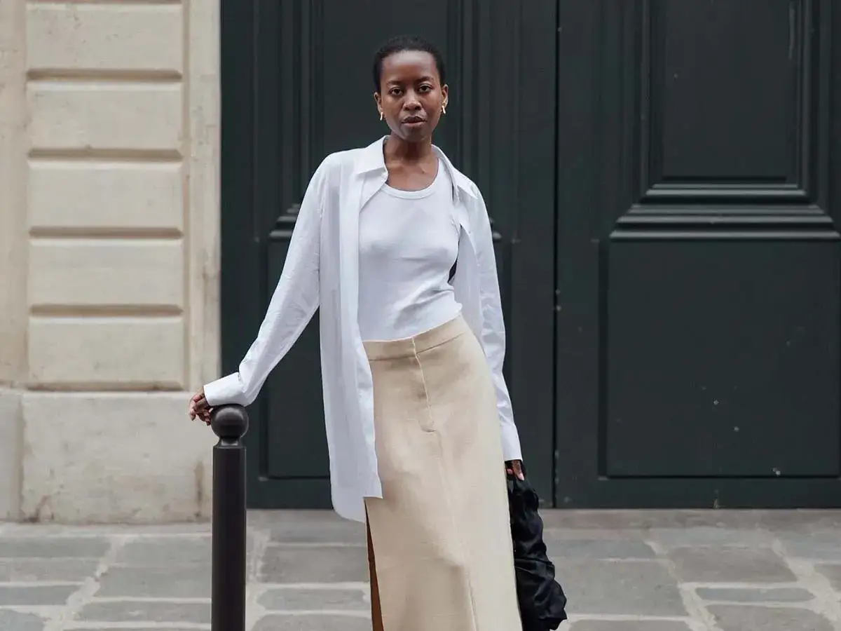 Mujer con un look minimalista, ideal para un armario cápsula. Falda beige y camisa blanca oversize.