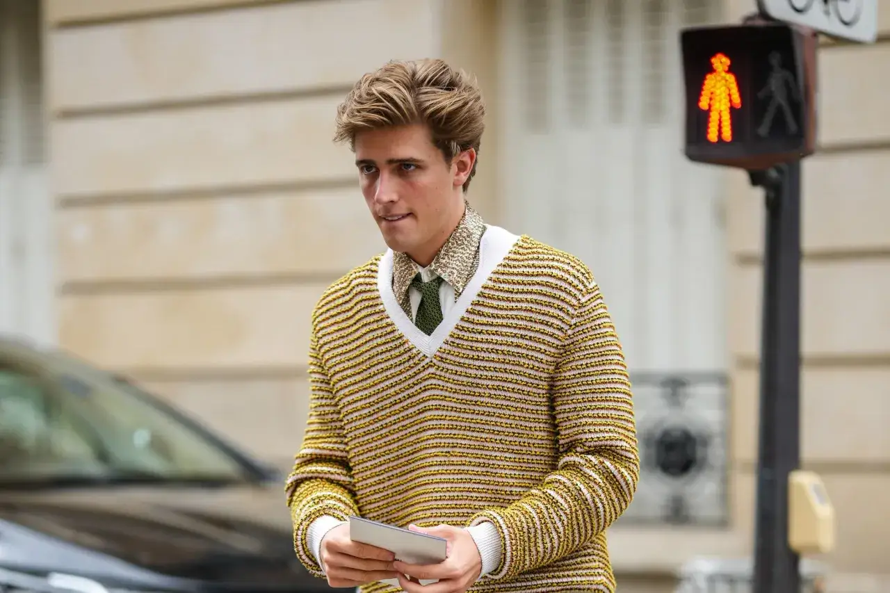 Joven con su&eacute;ter de rayas amarillas y blancas, camisa estampada y corbata verde. Un look casual old money con un toque moderno.