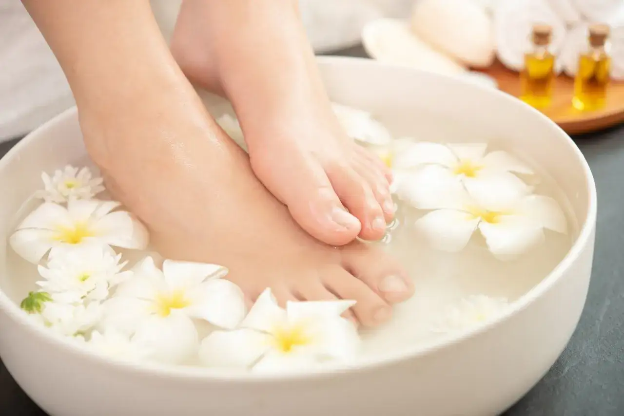 Pies sumergidos en agua con flores blancas, un ritual de spa para probar remedios caseros para quitar el mal olor de los pies.