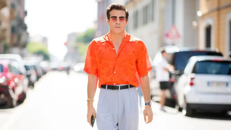Hombre con camisa naranja estampada y pantalones grises, luciendo un elegante french tuck.