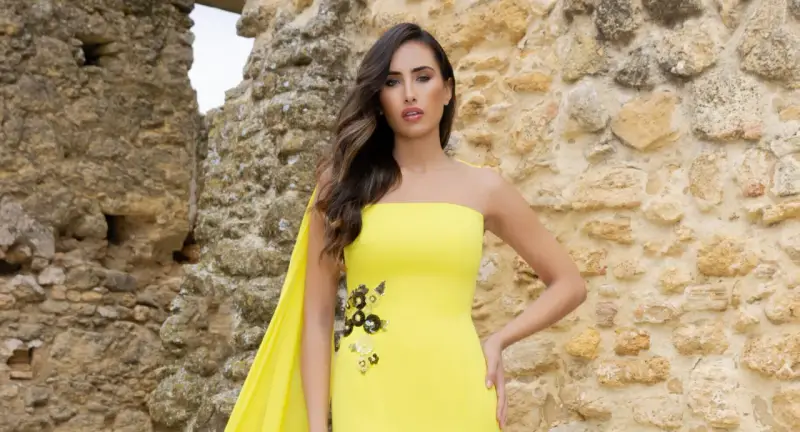 Mujer con vestido amarillo sin tirantes, con detalles florales y capa. Explora los diversos tipos de cuellos de vestidos.